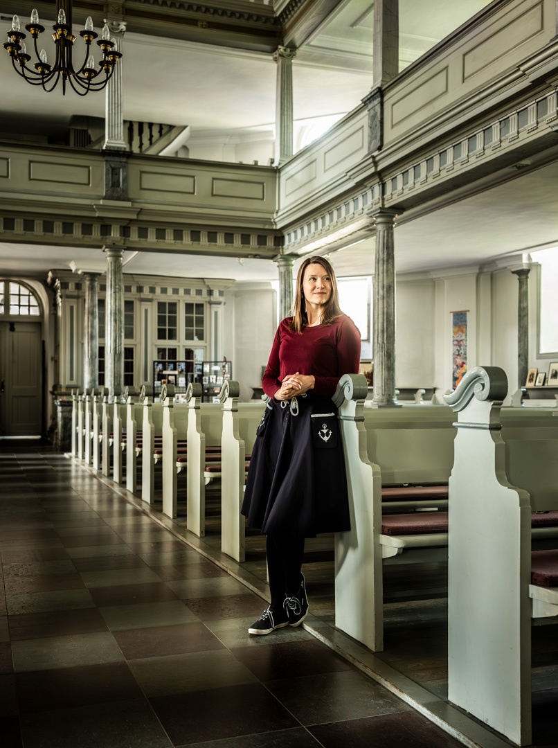 Eine Frau mit rotem Pullover und schwarzem Rock steht in einer Kirche