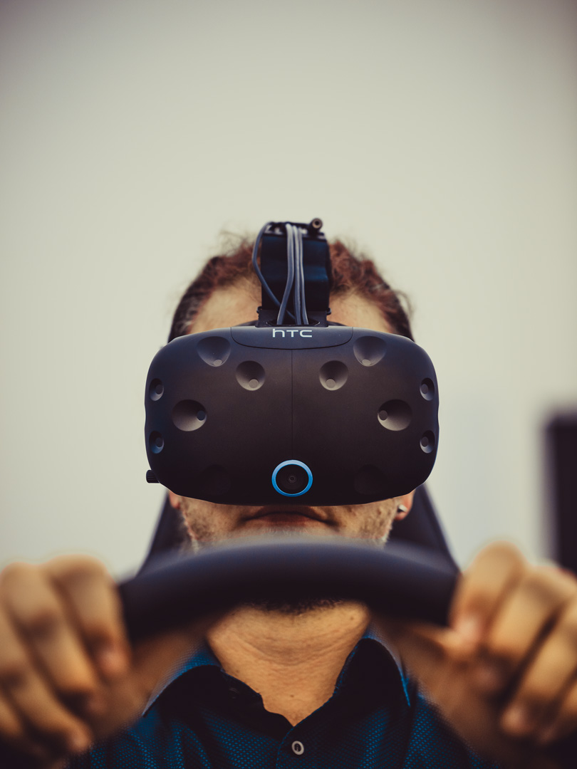Ein Mann mit VR-Brille hat seine Hände an einem schwarzen Lenkrad.